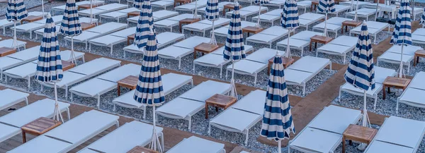 Row of beach sun beds with blue and white umbrellas await vacationers on a beach in France