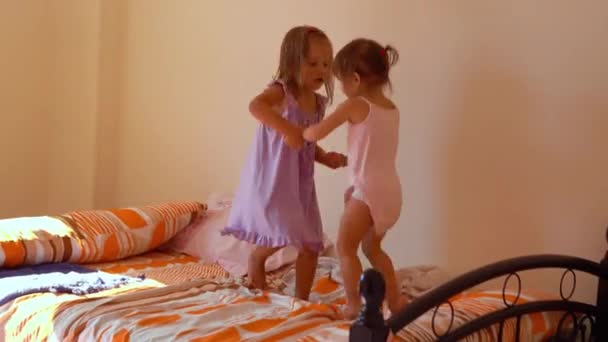 A nővérek ugrálnak az ágyon, játszanak és nevetnek. — Stock videók