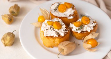 Ricotta bruschetta ve beyaz tabakta Physalis meyveleri.