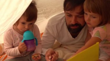 Baba ve küçük kızları çadırda kitap okuyorlar. 