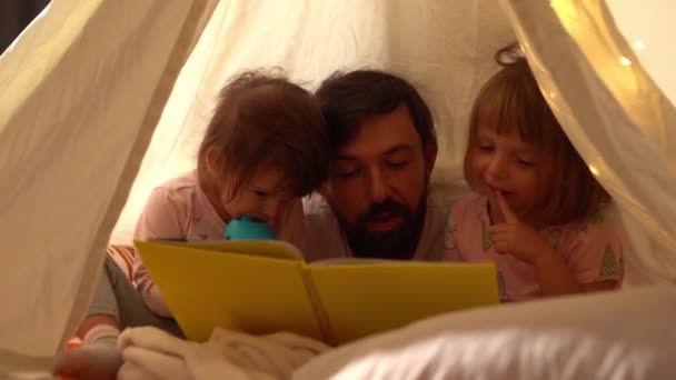 बाबा आणि लहान मुली टीपी तंबूमध्ये पुस्तक वाचत — स्टॉक व्हिडिओ