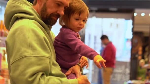 Маленька дівчинка вибирає цукерки з татом в цукерковому магазині — стокове відео