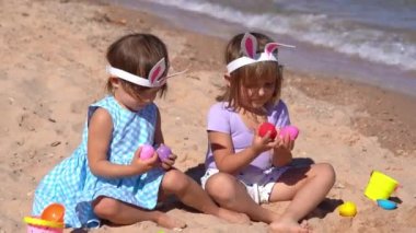 İki küçük kız sahilde paskalya yumurtalarıyla oynuyorlar. 