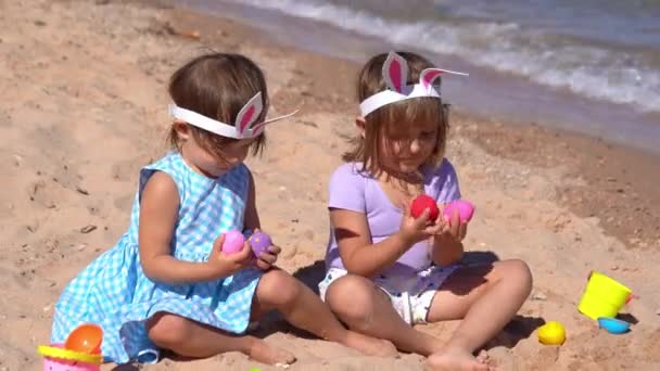 İki küçük kız sahilde paskalya yumurtalarıyla oynuyorlar. — Stok video
