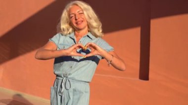 Olgun sarışın kadın hava öpücüğü yolluyor, el işareti kalp şeklinde. 