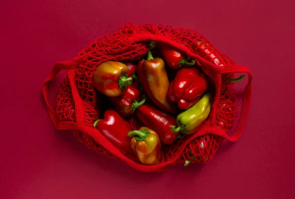 Frische Paprika in umweltfreundlicher Tasche auf rotem Hintergrund. — Stockfoto