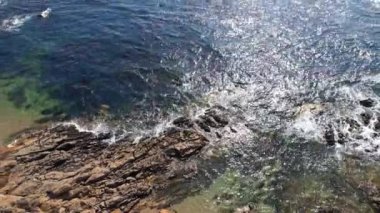 Güzel hava manzaralı dalgalar mavi bir okyanusta kayalara çarpıyor. Kuş bakışı okyanus dalgaları boş bir taşa çarpıyor. 