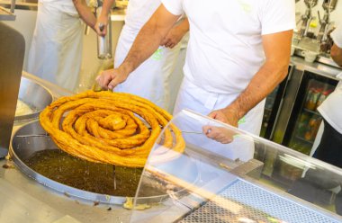 Pişirme yağında churros pişiren bir adam, sıcak yağda pişirilmiş churros 'u yakına getirir.