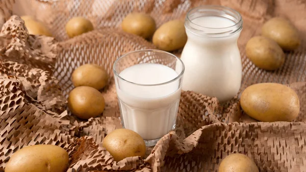 A glass and bottle with potato milk with the potato tubers. Vegan trend in healthy eating. Alternative plant milk