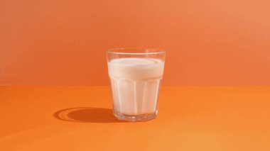 Glass with milk on orange background, creative minimalism and healthy food concept