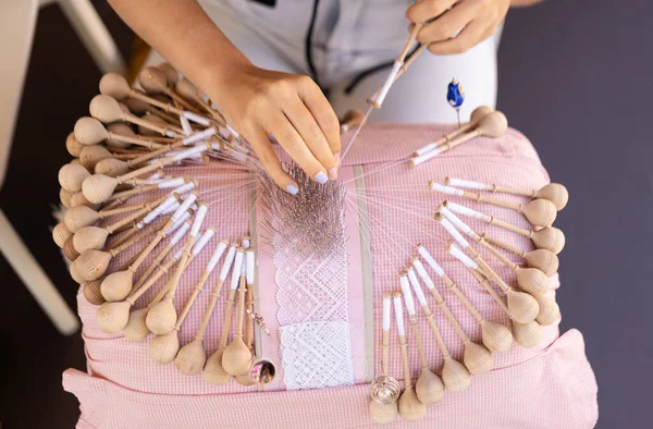 Bobbin lace handcrafting. Close-up of female hands braiding threads to make a pattern. Using threads and bobbins and needles according to the pattern.