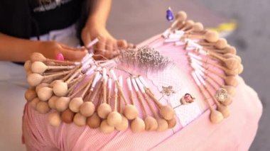 Close-up of female hands braiding threads to make a pattern. Using threads and bobbins and needles according to the pattern. Bobbin lace handcrafting. 