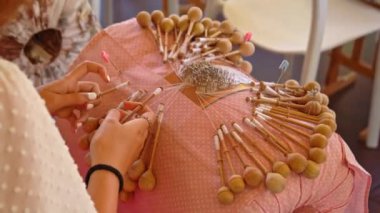 Bobbin lace handcrafting. View from behind of female braiding threads to make a pattern. Using threads and bobbins and needles according to the pattern.