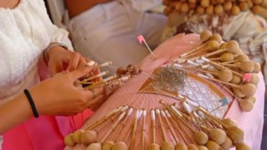 Bobbin lace handcrafting. Close-up of female hands braiding threads to make a pattern. Using threads and bobbins and needles according to the pattern.