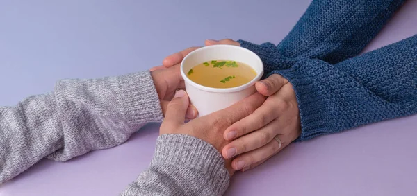 Famele hands gives a Chicken broth soup in paper cup to enother person.