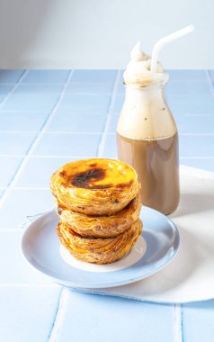 Stack of egg tart dessert Pasteis Pastel de nata or Pastels de Belem with a coffee cocktail on the blue tile table. Selective focus