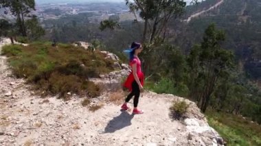 Young woman with blue hair alone on the mountain peak in summer. Circle Aerial view of a beautiful mountain canyon and tourist