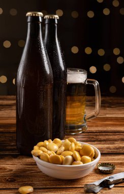 Kahverengi şişeden bardağa servis edilen bira ve ahşap bar masasında bokeh ışıkları olan bir kase tuzlanmış lupin.