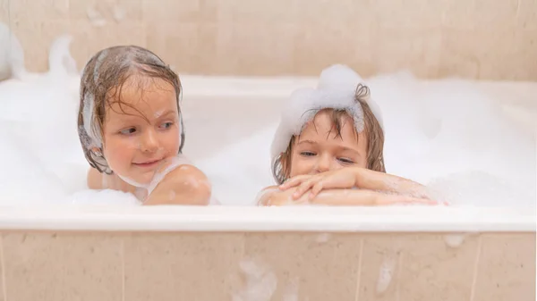 Funny sisters - baby girls playing with Soap Foam in the bath. Fun and children hygiene concept