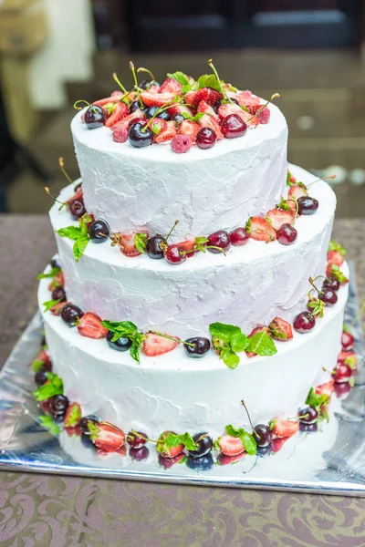 White wedding cake decorated by flowers standing on festive table with lots of snacks on side. Violet flowers on foreground. Wedding. Recetion