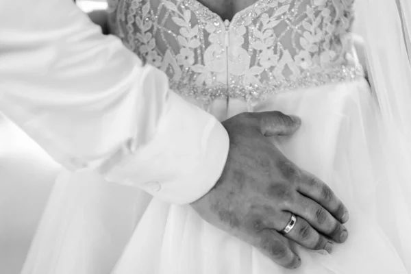 Bridal morning, bride wears dress. Groom helping fiancee to get dressed, adjusting buttons on wedding gown, rear view. close-up, crop