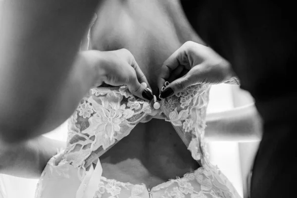 Bridal morning, bride wears dress. Groom helping fiancee to get dressed, adjusting buttons on wedding gown, rear view. close-up, crop