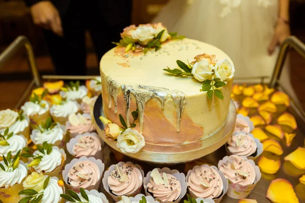 White wedding cake decorated by flowers standing on festive table with lots of snacks on side. Violet flowers on foreground. Wedding. Recetion