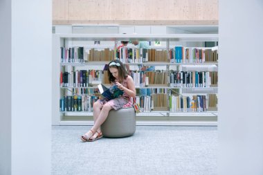 Barcelona 'daki Gabriel Garcia Marquez Halk Kütüphanesinde Pouf okuyan bir kız. Düzenleyicinin metni için boş kopyalama alanı.