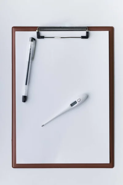 Top view of pen-type digital thermometer, ballpoint pen and brown clipboard with blank sheet of paper for your design. Clear white background. Healthcare concept.