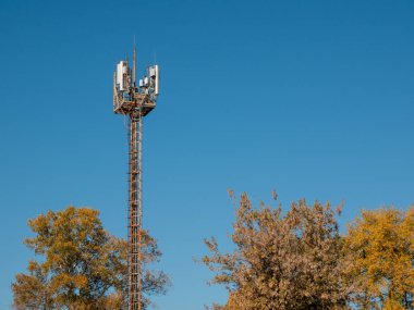 Farklı cep telefonu operatörlerinin iletişim antenlerine sahip bir kule. Parlak mavi gökyüzünün arka planına karşı.