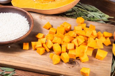 İtalyan Vejetaryen Balkabağı Risotto 'su için malzemeler - Kasede pirinç, kesme tahtasında balkabağı parçaları, ve adaçayı