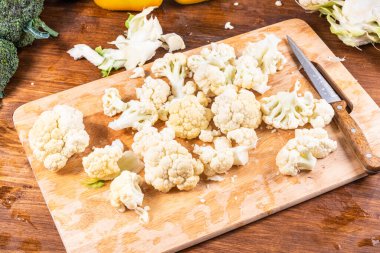 Mutfak masasında bıçakla kesilmiş karnabahar ve sebzeler.