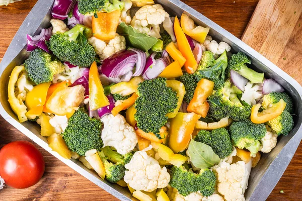 Cauliflower, broccoli, peppers and onions cut into pieces in a baking tray, top view