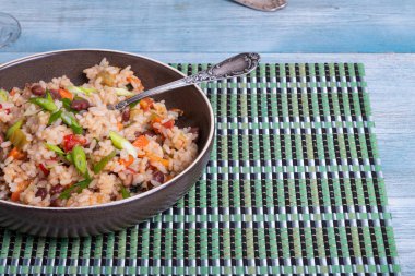 Fried rice with vegetables and beans with glazed onions in a plate with a fork on the table