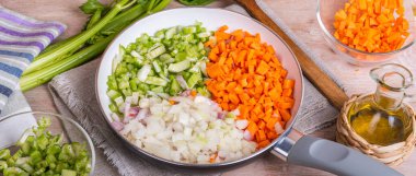 Preparation of the Italian classic base for dishes - soffritto. Finely chopped onions, carrots and celery in a skillet on the table with ingredients. Culinary background for Italian cuisine - soffritto.