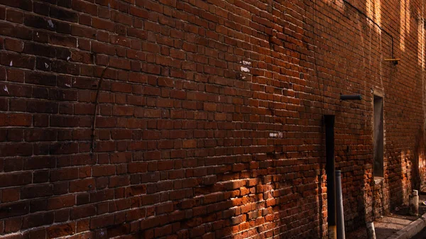 Wall of an old red brick house with patches of light