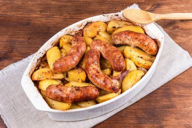 Seramik fırın kabında sosisli fırında patates, üst manzara, kaşıkla.