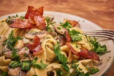Mantar soslu fettuccine, kızarmış pastırma ve taze maydanoz tabakta, yakın plan - klasik İtalyan makarnası.
