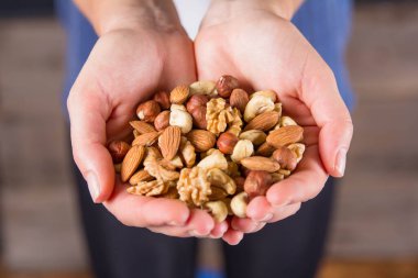 Soyulmuş badem, ceviz ve fındık dolu dişi avuçlar.