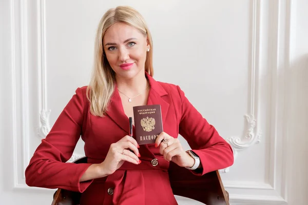 Kırmızı elbiseli çekici sarışın kadın Rusya Federasyonu vatandaşının ulusal pasaportunu elinde tutuyor. Kırmızı elbiseli bir kadının ellerinde Rus pasaportu ve kalemi vardı..