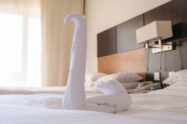 Otel odasındaki yataktaki beyaz havlu kuğusundan katlanmış. Otel müşterilerinin odalarını temizlerken geleneksel dekorasyon..