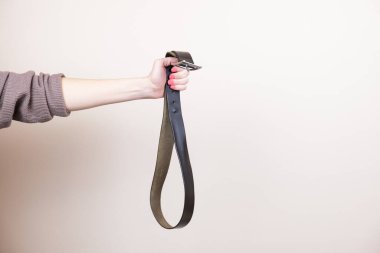 Kadının eli, metal tokalı deri bir pantolon kemeri tutuyor. Çocuklara fiziksel ceza konsepti, istismar metaforu. Metin eklemek için boşluk.