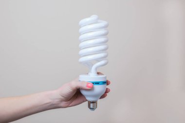 Bir kadın eli büyük bir enerji tasarrufu lambası tutar. Enerji tasarrufu kavramı, çevre dostu yaşam tarzı. Ekonomik aydınlatma lambalarının kullanımı.