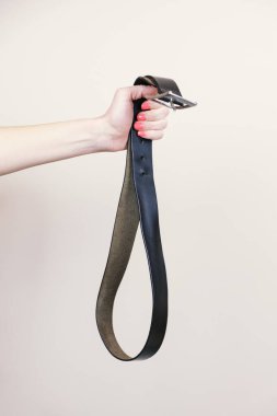 Kadının eli, metal tokalı deri bir pantolon kemeri tutuyor. Çocuklara fiziksel ceza konsepti, istismar metaforu. Dikey resim