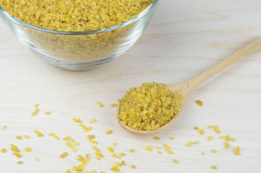 Bulgur ahşap kaşık ve cam kase içinde inliyor. Geleneksel bulgur yemeği hazırlama. Sağlıklı yiyecekler, hızlı karbonhidratlar. Haşlanmış, kurutulmuş ve ezilmiş buğdaydan yapılan kuru Groats..