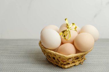 Straw basket with chicken eggs lying in it. One of the eggs is tied with a festive gold ribbon. Farm chicken eggs produced in your own chicken coop. Preparation for the celebration of Easter.