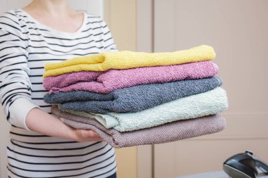 Woman holds a stack of clean terry towels. Folding clean linen, cleaning the house, caring for home textiles. Taking care of the family.
