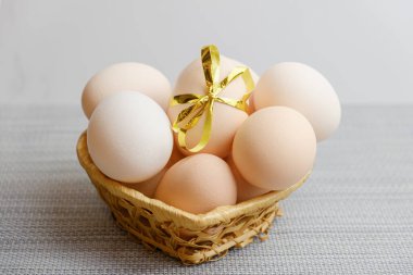 Straw basket with chicken eggs lying in it. One of the eggs is tied with a festive gold ribbon. Farm chicken eggs produced in your own chicken coop. Preparation for the celebration of Easter.