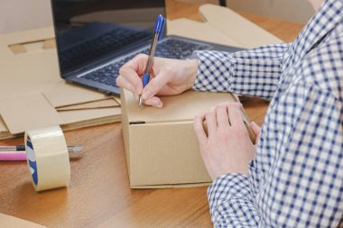 Resepsiyondaki kadın, e-ticaret siparişini karton bir kutuda kalemle işaretliyor. Depo çalışanlarının işlemleri ve teslimat siparişleri, depo malları lojistiği.