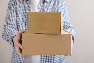 Courier in a check shirt holds out a two sealed cardboard boxes. Delivery of online orders. The delivery clerk brought the packaged order. Space for text.